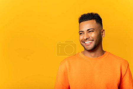 Photo for Portrait of happy satisfied handsome young Indian man standing with smile and looking away. Indoor studio shot on yellow background - Royalty Free Image