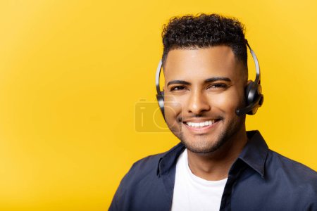 Foto de Sonriente joven trabajador de oficina indio en gafas y auriculares mirando a la cámara y sonrisas, hombre positivo que trabaja en el departamento de servicio al cliente, aislado en amarillo - Imagen libre de derechos