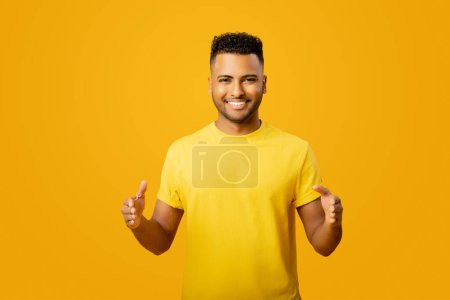Photo for Young handsome Arab man measuring empty space, showing size standing isolated on yellow, cheerful indian man holding hands in front of him, sizing wide - Royalty Free Image