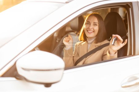 Téléchargez les photos : Femme joyeuse montrant la clé de la nouvelle voiture, assis à l'intérieur regarde la caméra et souriant, femme à succès acheter une voiture - en image libre de droit