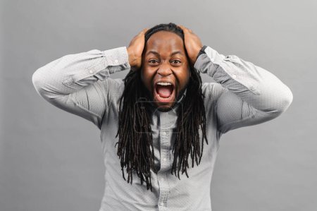 Téléchargez les photos : Homme afro-américain fou avec dreadlocks regardant la caméra et hurlant, homme effrayé isolé sur gris - en image libre de droit