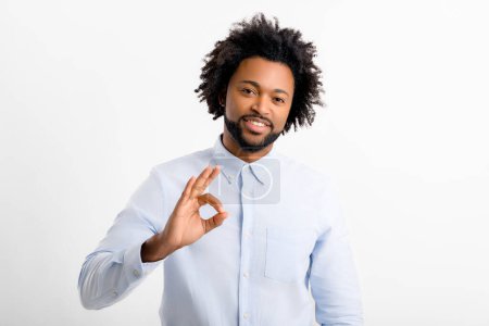 Téléchargez les photos : Bouclé sourire joyeux homme afro-américain trentenaire portant chemise de bureau formelle montrant ok geste isolé sur fond blanc, approuvant - en image libre de droit