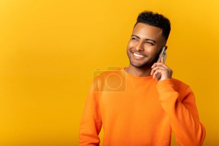 Photo for Indian man talking phone, calling to somebody, looking away with happy facial expression. Indoor studio shot isolated on orange background - Royalty Free Image