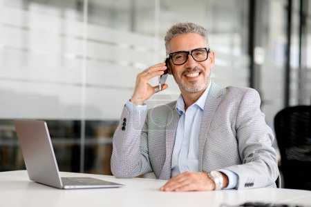 Photo for Headshot of handsome charismatic mature businessman talking on smartphone sitting at the office desk, middle-aged 50s man in formal wear having phone conversation with customers or business partners - Royalty Free Image