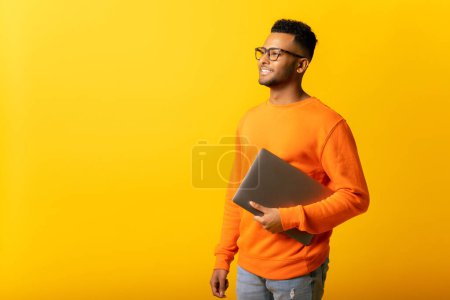 Photo for Inspired indian male office employee or student carrying laptop isolated on plain yellow color, handsome arab man full of new ideas looking aside thoughtfully, start-up owner - Royalty Free Image
