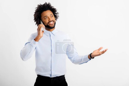 Téléchargez les photos : Toujours en contact. Afro-Américain bouclé homme en chemise blanche formelle parler sur le smartphone et gestuelle, avoir des conversations avec des clients ou des collègues, studio tourné isolé sur blanc - en image libre de droit