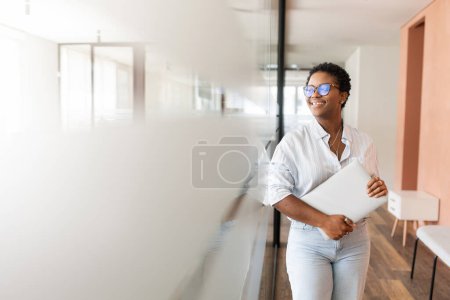 Téléchargez les photos : Portrait d'une jeune employée de bureau afro-américaine souriante et charismatique, femme avec une coupe de cheveux courte debout posant dans le couloir et regardant de côté, la stagiaire optimiste le premier jour de travail - en image libre de droit