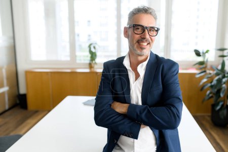 Photo for Headshot of high-skilled mature male employee standing with arms crossed in modern office, successful confident 50s businessman wearing eyeglasses, business portrait of senior 60s entrepreneur - Royalty Free Image