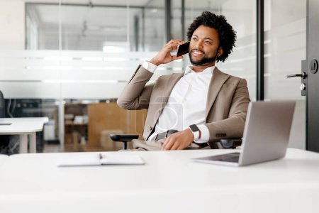 Foto de Un hombre de negocios afroamericano equilibrado está involucrado en una conversación telefónica en un entorno de oficina moderno, exudando confianza y profesionalismo. Su postura relajada y su sonrisa sugieren un diálogo positivo - Imagen libre de derechos