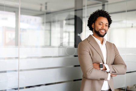 Téléchargez les photos : Un homme d'affaires afro-américain se tient avec confiance dans un environnement de bureau moderne, les bras croisés, exsudant un sens du leadership et l'assurance calme d'un professionnel chevronné - en image libre de droit