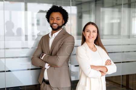 Photo for A man and a woman, both dressed in business casual attire, confidently stand with crossed arms in a modern office environment, exuding professionalism and partnership - Royalty Free Image