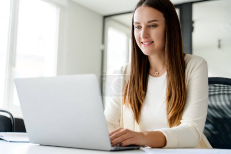 Photo for Focused and engaged a young businesswoman types away on a laptop at an office desk, focused female office employee responding emails sitting on the comfy well-organized workplace - Royalty Free Image