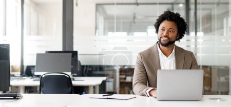 Photo for African-American young businessman working on his laptop in a contemporary office space with glass partitions on the backdrop. Concept of business and technology, bunner, panoramic view - Royalty Free Image