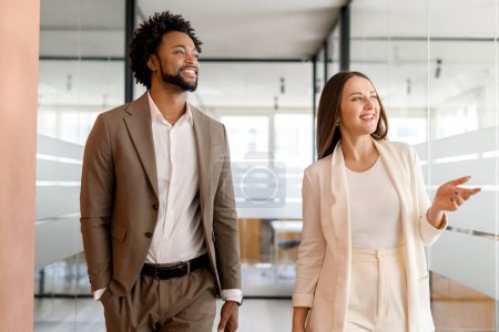 In a light-filled office, a man and woman walk together, engaging in a relaxed yet animated conversation that suggests a positive working relationship. Teamwork and a shared vision concept