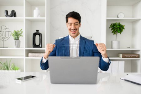 Photo for A jovial Hispanic businessman celebrates success or good news on his laptop in a sleek, contemporary office, exuding confidence and achievement. Concept of positive results in business - Royalty Free Image
