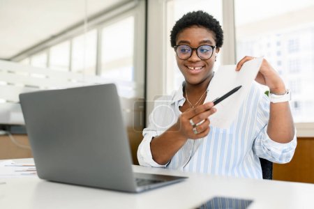 Photo for Diverse office employees concept. African-American woman using laptop for online video meeting, talking with colleagues or coworkers online, presenting business plan. Teacher conducting webinar - Royalty Free Image