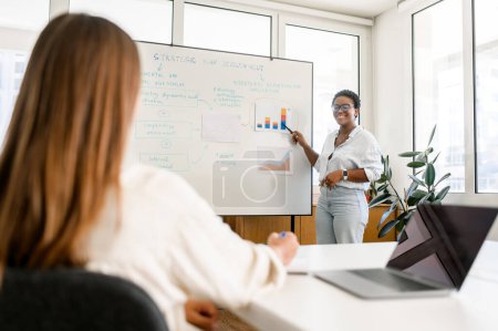Photo for Female entrepreneur, manager or colleague showing financial graphics or discussing diagrams on interactive whiteboard to female business partner or employee, presenting own project, coaching trainee - Royalty Free Image