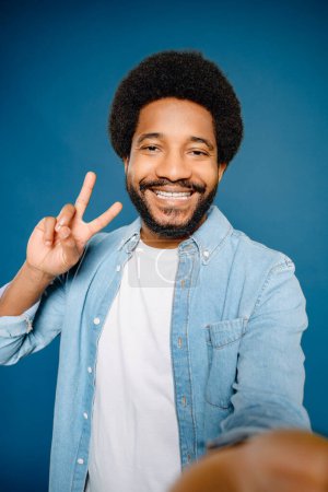 Photo for Cheerful Latin young man taking a selfie with a peace sign and a bright smile, the man showcases his fun-loving personality and a knack for creating engaging content for social media - Royalty Free Image