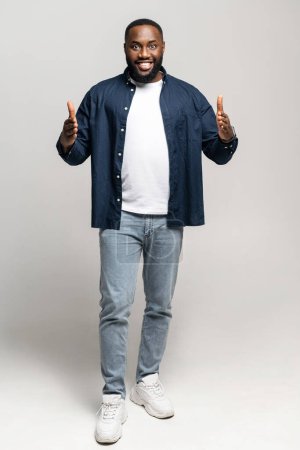 Portrait complet de l'homme afro-américain debout, les mains gesticulant un espace modéré, indiquant une taille ou une distance. Homme noir en tenue décontractée tenant l'espace vide pour la publicité, isolé sur blanc