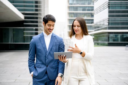 Photo for In a casual business exchange, a man and woman walk while discussing a project on a digital tablet, epitomizing on-the-go professionalism in an urban setting. - Royalty Free Image