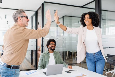 A high-five gesture between colleagues in a modern office space highlights a successful moment, with the surrounding team sharing in the jubilant spirit, a celebratory work environment