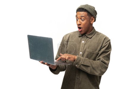Téléchargez les photos : Portrait d'un homme surpris choqué tenant un ordinateur portable et regardant l'écran avec de grands yeux étonnés. Studio intérieur tourné isolé sur fond blanc - en image libre de droit