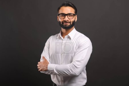Photo for Headshot of intelligent professional Indian businessman wearing formal wear and eyeglasses looking at the camera while posing arms crossed isolated on black - Royalty Free Image