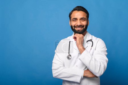 Téléchargez les photos : Un médecin indien joyeux en blouse blanche, son stéthoscope visible autour de son cou. Cette image respire le professionnalisme et la confiance, parfait pour illustrer les fournisseurs de soins de santé ou le personnel médical. - en image libre de droit