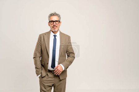 Photo for High-skilled senior businessman stands with one hand in his pocket, displaying a look of approachability and confidence against a light neutral background, perfect for corporate branding - Royalty Free Image