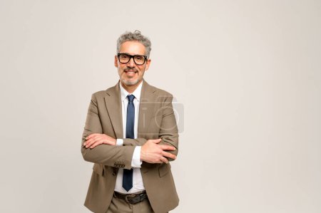 A senior businessman stands confidently with his arms crossed in a neutral background, embodying professionalism and experience with a friendly demeanor. Grey-haired mature professional isolated