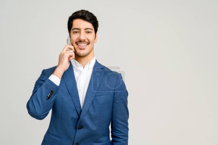 Foto de Retrato profesional de un hombre en un traje de negocios azul se dedica a una conversación telefónica, sonriendo y mirando a la cámara, lo que sugiere un diálogo empresarial exitoso o interacción con el cliente - Imagen libre de derechos