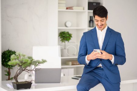Photo for The businessman checks his smartphone with a focused expression, standing in a minimalist office setup that underscores the efficient and tech-savvy nature of todays entrepreneurs - Royalty Free Image