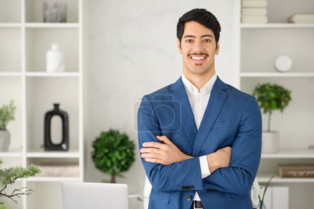 The cheerful businessman in a blue suit looking at the camera, radiating positivity and approachability in a well-organized workspace. Essence of friendly professionalism and accessibility