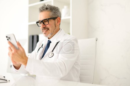 Un profesional médico senior está utilizando su teléfono inteligente, posiblemente accediendo a los datos del paciente o programando citas, lo que significa el papel de los teléfonos inteligentes en la accesibilidad sanitaria
