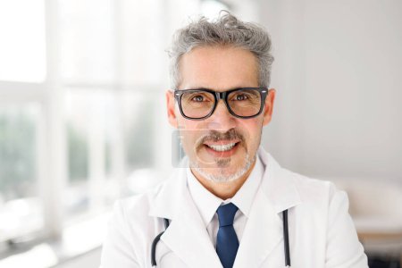 Portrait d'un médecin chevronné avec un sourire chaleureux, portant des lunettes et un stéthoscope, capturé dans un bureau bien éclairé qui communique un cadre de soins de santé accueillant et professionnel. Concept de soins de santé