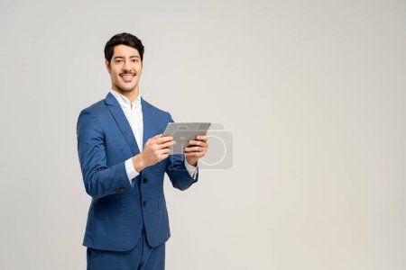 Téléchargez les photos : Un homme en costume bleu utilise avec confiance une tablette, son sourire transmettant facilité et expertise avec la technologie, concept de communications d'affaires, solutions numériques, et la gestion d'entreprise facilitée par la technologie - en image libre de droit