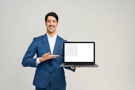 Photo for Man in a smart blue suit stands against a clean background, holding a laptop with a blank screen towards the camera, the perfect template for graphic designers to superimpose an application or website - Royalty Free Image