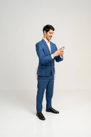Photo for Young Hispanic businessman in a blue business suit using a smartphone with an engrossed expression, reading an important message or browsing business content, concept of business and technology - Royalty Free Image