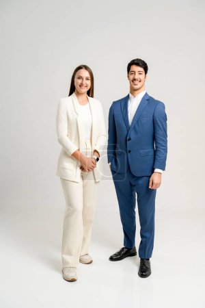 Foto de Dos profesionales en un ambiente de negocios, una mujer en traje de crema y un hombre en traje azul, están de pie con confianza, lo que refleja un exitoso dúo de negocios listo para la colaboración y el liderazgo. - Imagen libre de derechos