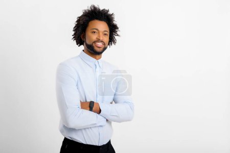 Foto de Sonriente hombre de negocios afroamericano barbudo de pie con los brazos cruzados y mirando a la cámara. Orgulloso y exitoso dueño de una pequeña empresa, gerente aislado en blanco - Imagen libre de derechos