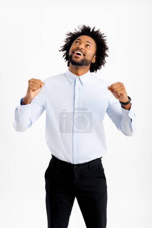 Téléchargez les photos : Heureux heureux afro-américain employé de bureau masculin levant les poings serrés en signe de victoire, heureux homme noir en tenue formelle célébrant le succès ou une bonne affaire, levant les yeux et remerciant Dieu - en image libre de droit