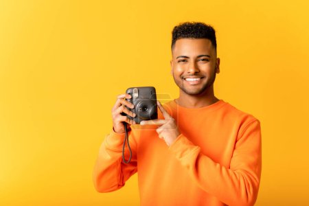 Photo for Say cheese. Studio portrait of young Indian man photographer making photo with polaroid camera. Handsome cheerful arab guy with instant photo camera looking at you - Royalty Free Image