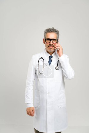 Téléchargez les photos : Dans ce portrait, le médecin mature est engagé dans un appel téléphonique, discutant éventuellement des soins aux patients, soulignant l'importance de l'accessibilité en médecine. - en image libre de droit