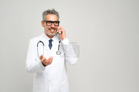 Photo for A mature, grey-haired doctor with a friendly expression is engaging in a phone conversation, discussing a patients treatment plan, highlighting the personal touch in modern medical consultations - Royalty Free Image