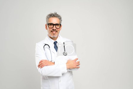 Photo for With a friendly smile and a professional demeanor, this senior doctor exudes approachability and experience, standing ready in a white lab coat with a stethoscope against a clean, white backdrop. - Royalty Free Image
