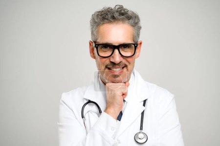 Téléchargez les photos : Cette image capture un médecin chevronné portant des lunettes, posant le menton posé sur sa main, signalant sa disponibilité à s'engager et à écouter les préoccupations des patients.. - en image libre de droit