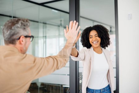 Photo for The colleagues exchange a high-five, their smiles reflecting a culture of achievement and mutual respect in a bright, modern office setting. The action signifies a successful collaboration - Royalty Free Image