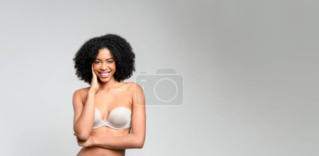 African-American woman laughs, stands in a strapless top, her arms crossed in a relaxed manner, against a neutral backdrop, encapsulating the spirit of carefree elegance and infectious cheerfulness