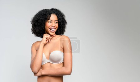 Foto de Una mujer afro-americana alegre con rizos y una sonrisa radiante toca su rostro tiernamente. El telón de fondo acentúa su risa espontánea y la felicidad infecciosa que irradia de ella. - Imagen libre de derechos