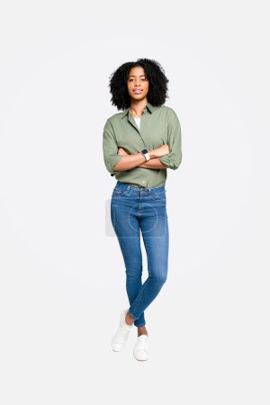 Una mujer afroamericana con camisa de olivo y vaqueros azules, de pie con confianza y una sonrisa graciosa, perfecta para temas de profesionalismo moderno y liderazgo accesible, larga duración